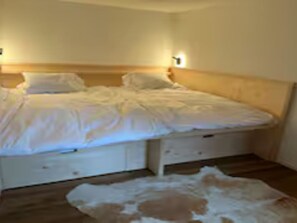 A bedroom with a wooden headboard, a bed with white bedding, and a small rug on the floor. - Baren Penthouse Appartement/Fewo, Dusche, WC 8-Bettwohnung by Interhome (Zweisimmen)