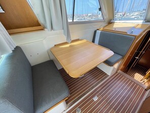 A compact interior with a bench, a small table, and a window with a view of boats. - Sun-Kissed Sailing Adventure in Zadar, Croatia (Bibinje)