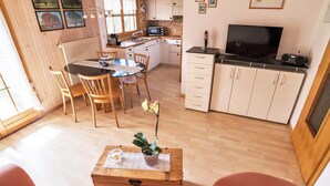 Ein gemütliches Wohnzimmer mit einem Holztisch, ein Essbereich mit einem Glastisch und eine Küche mit weißen Schränken und einem Fernseher.