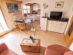 Ein gemütliches Wohnzimmer mit einem Holztisch, ein Essbereich mit einem Glastisch und eine Küche mit weißen Schränken und einem Fernseher.