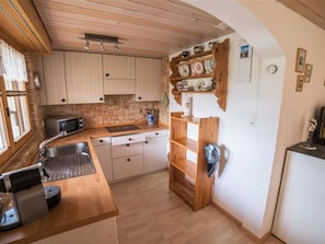Eine kleine Küche mit Holzausstattung, einer integrierten Mikrowelle und einem Spülbecken.