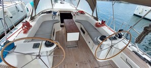 Ein Bootsdeck mit Steuer, einem kleinen Tisch und einer Sitzgelegenheit.