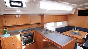 Una cocina compacta con fregadero, estufa y horno, un pequeño espacio de estar con mesa, y un televisor montado en la pared.