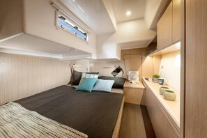 Un interior compacto y bien iluminado con una cama, mesita de noche y un ventanal pequeño.