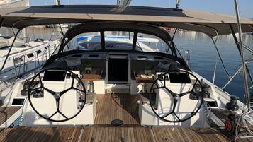 A boat's deck with a steering wheel, control panel, and seating area.