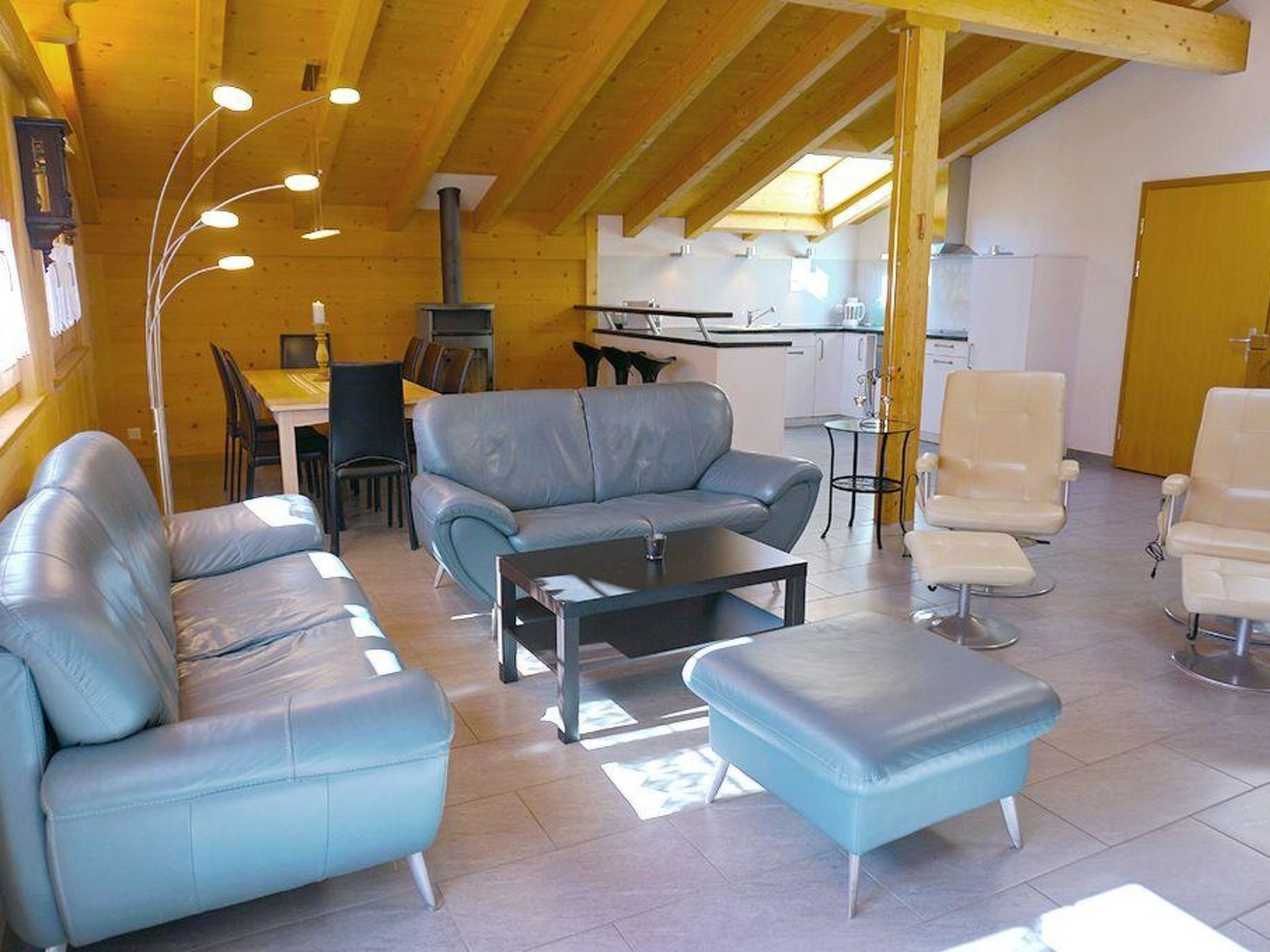 Een moderne woonkamer met een bank, poef en salontafel. Er is een eethoek met stoelen en een tafel, en een keuken op de achtergrond.