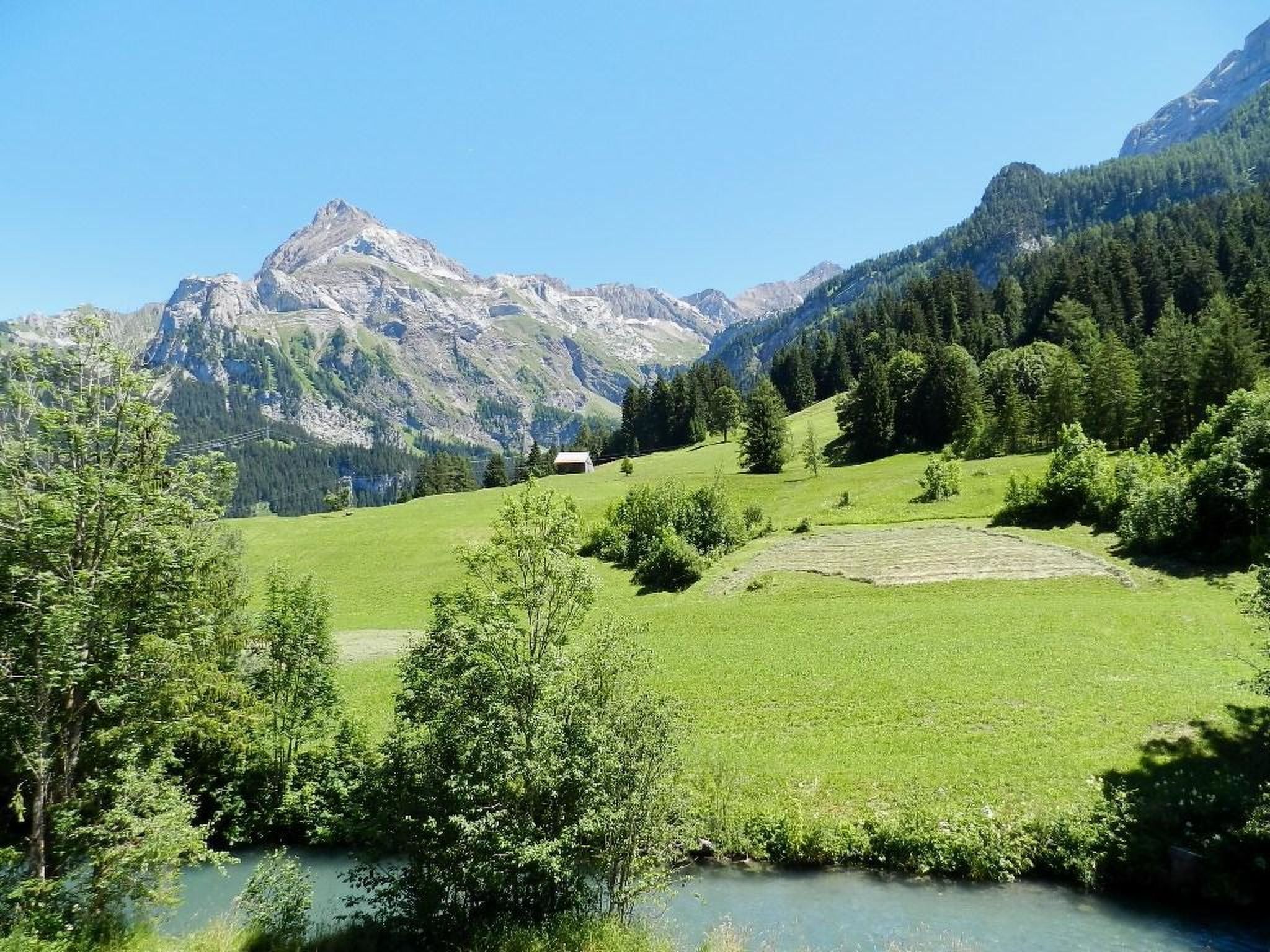 Un paysage de montagne avec un ciel dégagé, un petit bâtiment et une rivière.