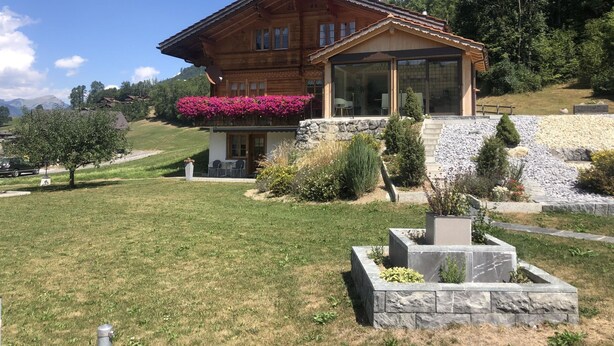 Eine Holzhütte mit Balkon, Steinmauern und einem Garten.