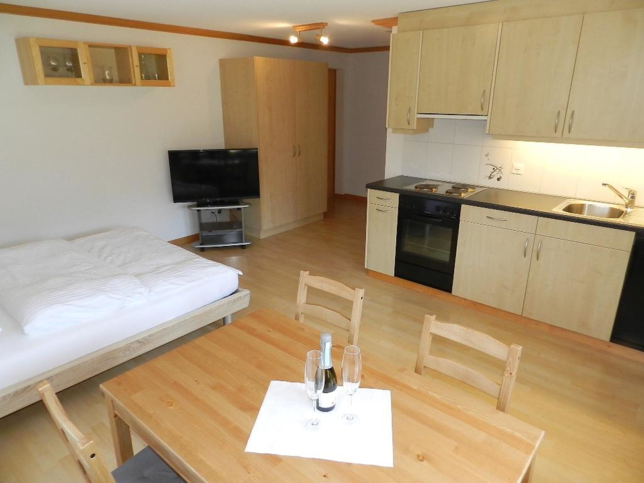 Ein kleines Hotelzimmer mit Bett, Fernseher, Küchenzeile und Essbereich.