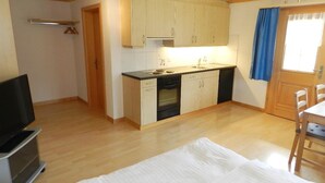 Eine kleine Küche mit Holzschränken, einem eingebauten Ofen und einer Essecke mit Tisch und Stühlen.