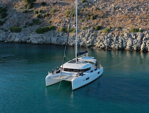 Eine weiße Yacht liegt an einer felsigen Küste mit klarem, türkisblauem Wasser.