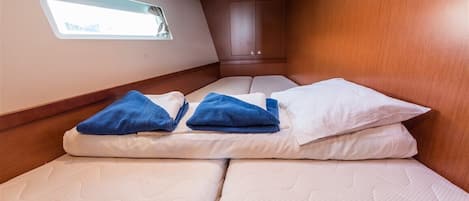 Ein kleines Häuschen mit einem schmales Fenster, einer Holzkabine und einem Bett mit weißer Bettwäsche und blauen Handtüchern.