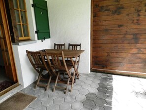 Een patio met een zeshoekig betegeld terras, een houten tafel en stoelen.