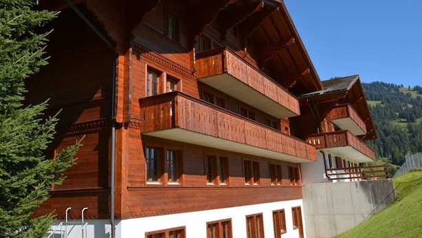 Un edificio in legno a più piani con balconi, una parte inferiore bianca e uno sfondo collinare.