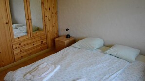 Una camera da letto con un'armadietto in legno, un comodino con una lampada e un letto con cuscini e un asciugamano piegato.