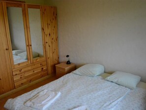 Ein Schlafzimmer mit einem Holzschrank, einem Nachttisch mit Lampe sowie einem Bett mit Kissen und einem gefalteten Handtuch.