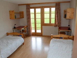 Une chambre avec deux lits, un bureau et une chaise. Il y a une fenêtre avec des rideaux.