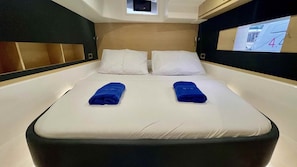 Ein Hotelzimmer mit Bett, zwei Kissen, einem Kopfteil, einem kleinen Fenster und einem an der Wand montierten Fernseher.