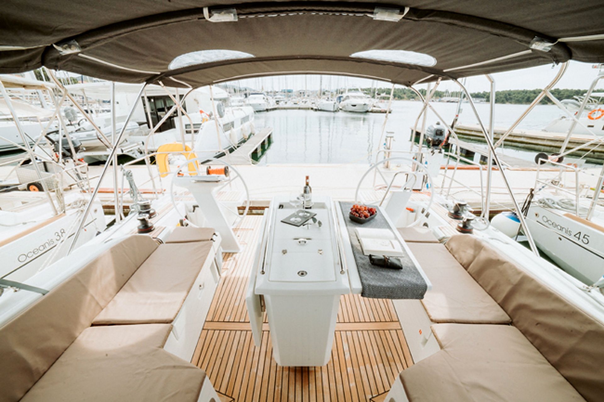 Une terrasse couverte dotée d’une table centrale, de sièges confortables et offrant une vue sur le port de plaisance et les bateaux.