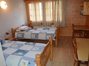 Ein Zimmer mit zwei Betten, einem Holztisch und einem Stuhl.