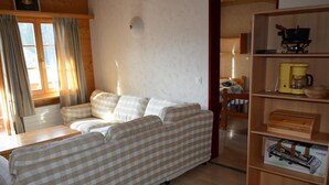 Un área de estar acogedora con un sofá de estampado vichy, una mesa de centro de madera y una estantería con diversos objetos.