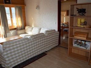 Ein gemütlicher Wohnbereich mit einem karierten Sofa, einem Holztisch und einem Bücherregal mit verschiedenen Gegenständen.