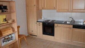Una cocina con armarios de madera, una estufa negra, un lavaplatos y una silla.