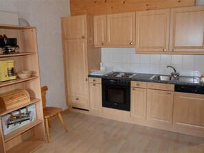 Eine Küche mit Holzausstattung, einem schwarzen Herd, einer Spüle und einem Stuhl.