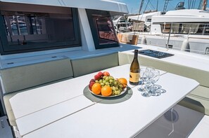Ein Esstisch mit Obstplatte, Weinflasche und Gläsern auf dem Deck einer Yacht.