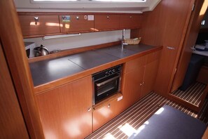 A compact kitchen with wooden cabinets, a stainless steel countertop, a built-in oven, and a window above the sink. - Sibenik Sun-soaked Sailing: A Luxurious Croatian Voyage (Pirovac)