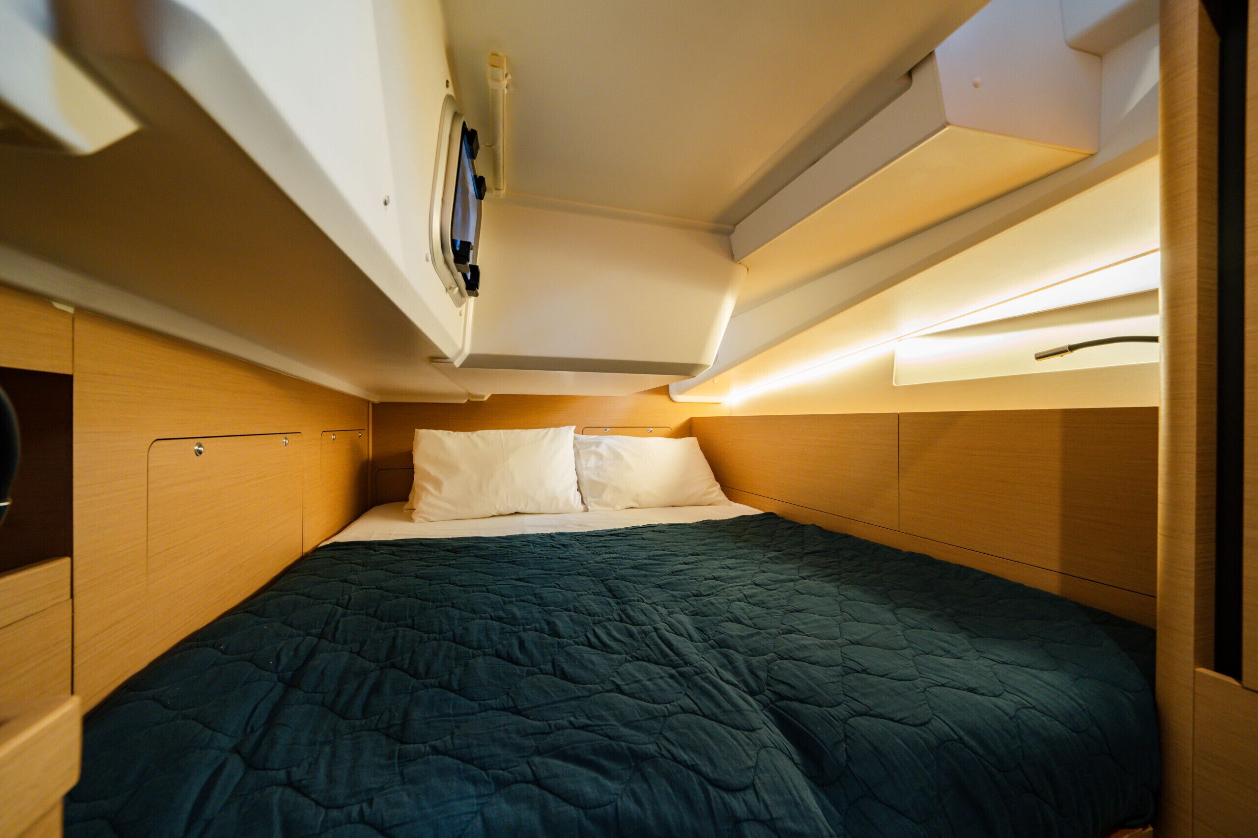 A compact, well-lit cabin with a single bed, built-in storage, and a small overhead shelf.