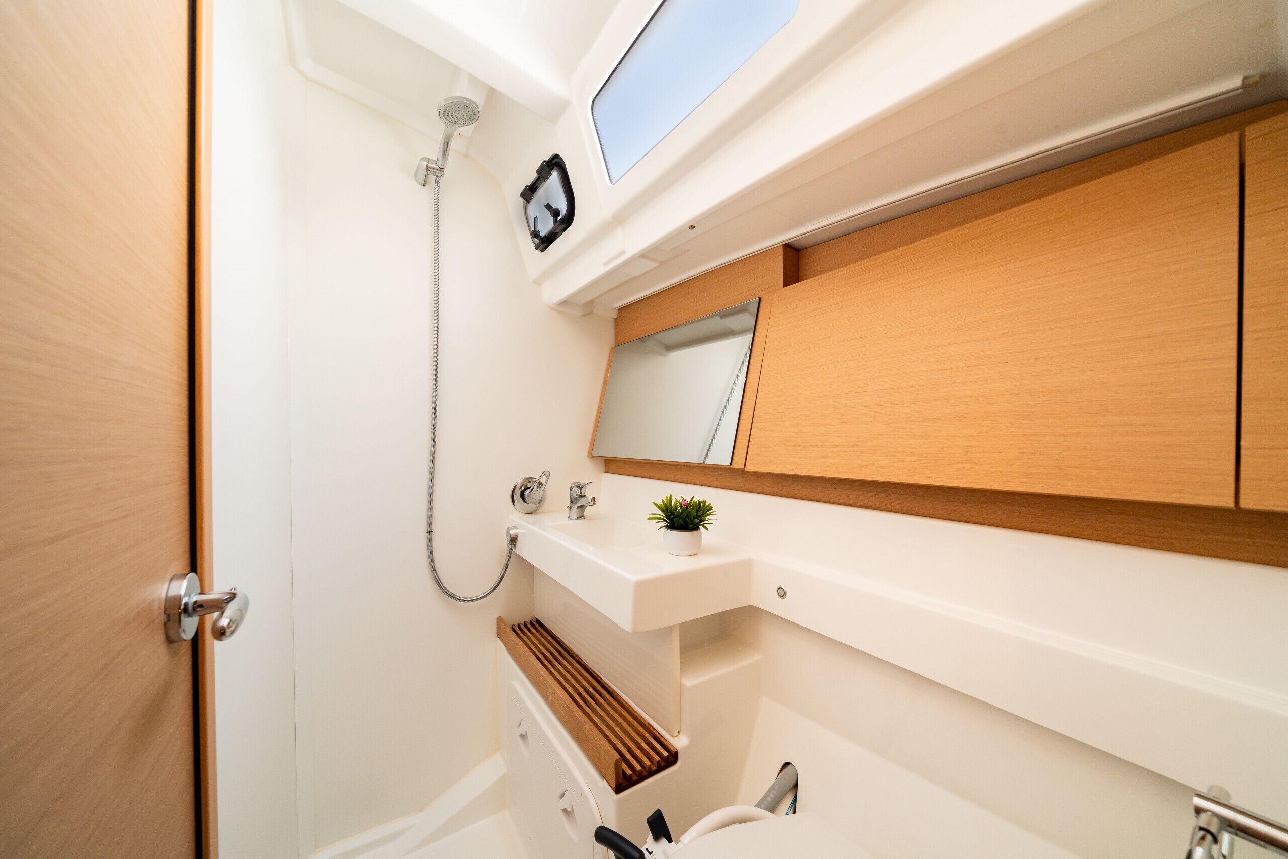 A compact bathroom with a wooden vanity, a small sink, a mirror, and a shower.
