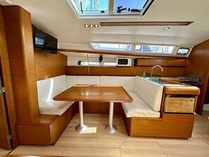 A compact galley with a wooden table, white cushioned seating, a microwave, and a sink. - Sun-Kissed Sailing Adventure in Zadar, Croatia (Drage)