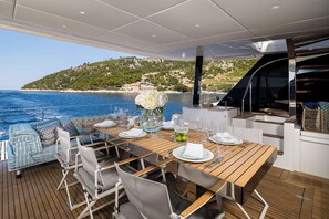 A dining area with a wooden table set for four, overlooking a coastal landscape. - Sun-Kissed Sailing Adventure in Split, Croatia (Kaštel Gomilica)