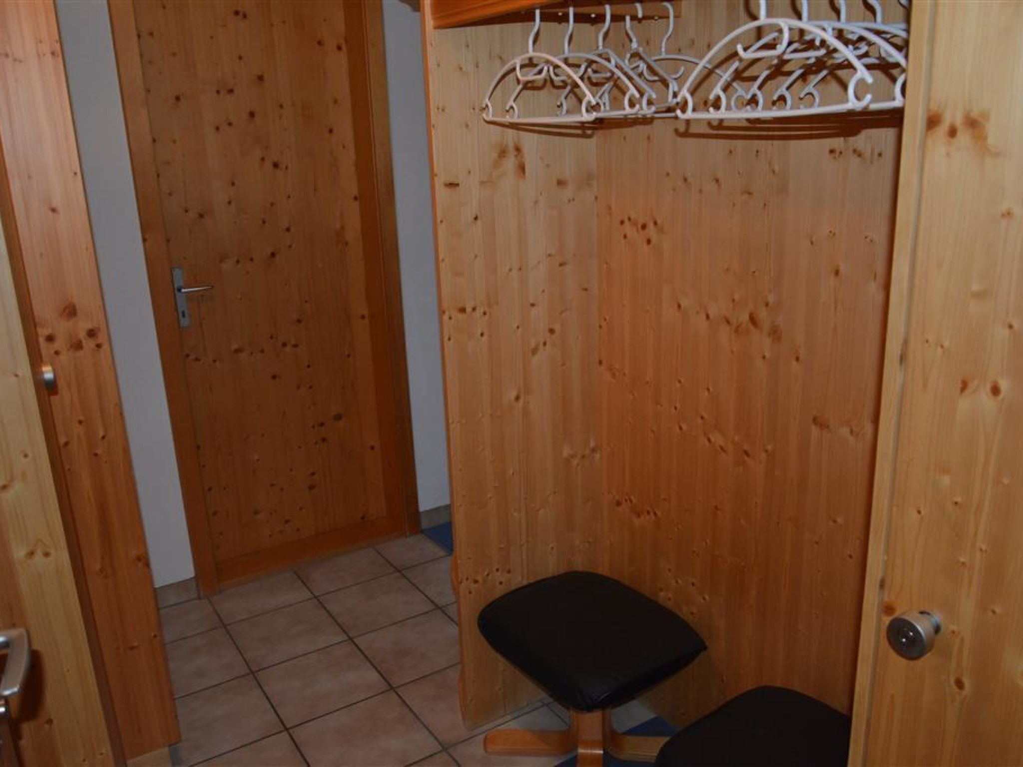Une pièce en bois avec une porte, un banc et un étagère en métal.