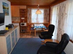 A compact living space with a kitchenette, a dining table with chairs, a television, and a large window with curtains.