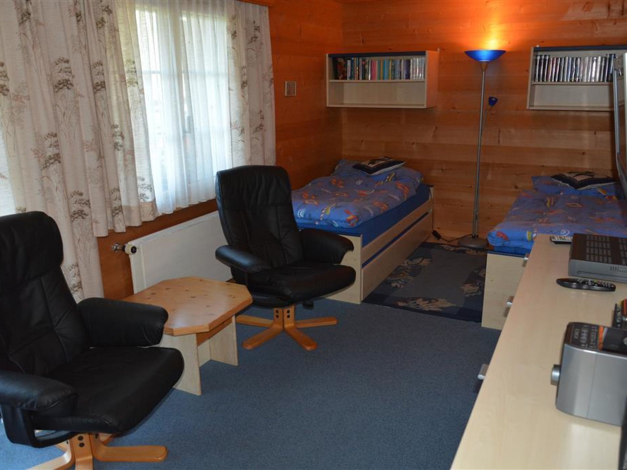 Ein kleines Zimmer mit einem Bett, einem Schreibtisch, einem Sessel und einem Bücherregal.