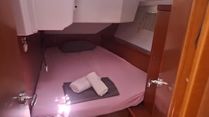 A small, single-bed room with a pink bedspread, a folded towel, and a wooden door.