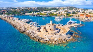 A coastal town with a historic fort, clear blue waters, and a marina with boats. - Sun-Kissed Sailing Adventure in the Dodecanese Islands (Rodos)