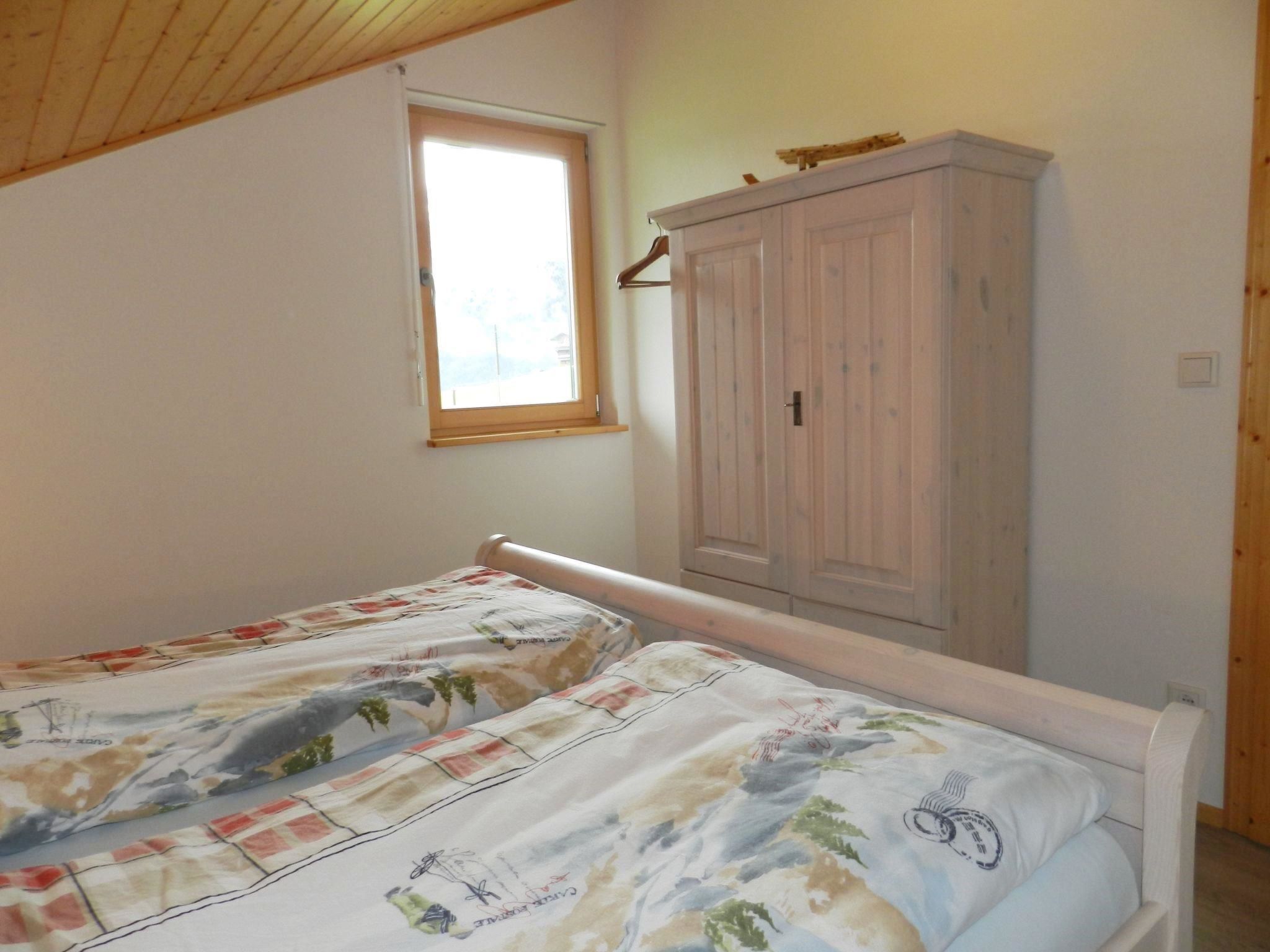 Een slaapkamer met twee eenpersoonsbedden, een kledingkast, een raam en een houten plafond.