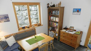 Una habitación acogedora con una mesa de madera, dos sillas, un sofá, una estantería y una ventana con vistas a la montaña.