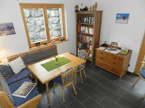 A cozy room with a wooden table, two chairs, a sofa, a bookshelf, and a window with a view of a mountain. - Panorama, Chalet Appartement/Fewo, Dusche oder Bad, WC 7-Bettwohnung by Interhome (Zweisimmen)