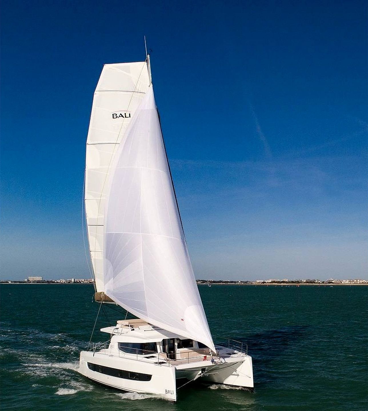 A sailboat with the name 'BAU' on its sail and hull, sailing on a body of water with a clear sky in the background.