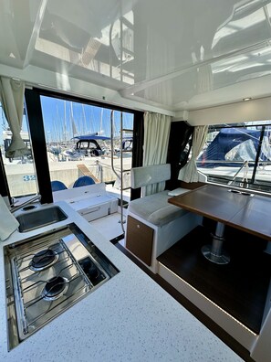 A boat interior with a kitchen area, seating, and a view of the marina. - Sun-Kissed Sailing Adventure in Zadar, Croatia (Drage)
