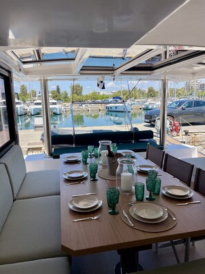 A dining area with a table set for four, a view of the marina outside, and a boat docked nearby. - Sun-Kissed Sailing Adventure in Islas Sarónicas (Alimos)