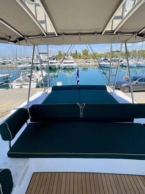 A boat deck with a view of a marina, a flag, and a car parked nearby. - Sun-Kissed Sailing Adventure in Islas Sarónicas (Alimos)