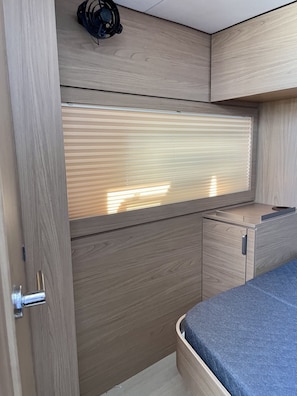 A compact room with a bed, a window with blinds, a small table, and a ceiling fan. - Sun-Kissed Sailing Adventure in Islas Sarónicas (Alimos)