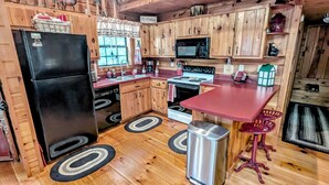Una cucina in stile baita con mobili in legno, un frigorifero nero, un forno a microonde, un fornello e un lavello.