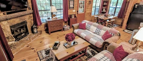 Interior acogedor de una cabaña con chimenea de piedra, mobiliario de madera y ventanas amplias.