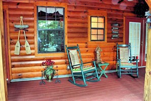 Eine Holzhütte mit Veranda, zwei Schaukelstühlen, einem Tisch und einem Schild, das auf ein Camp mit Annehmlichkeiten wie Kanuverleih, Bootsverleih, Feuerwerk und Wurm zum Angeln hinweist.